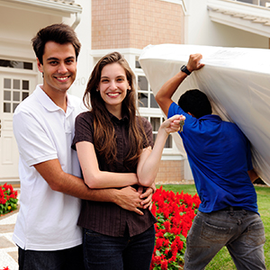 smiling couple with movers moving a mattress